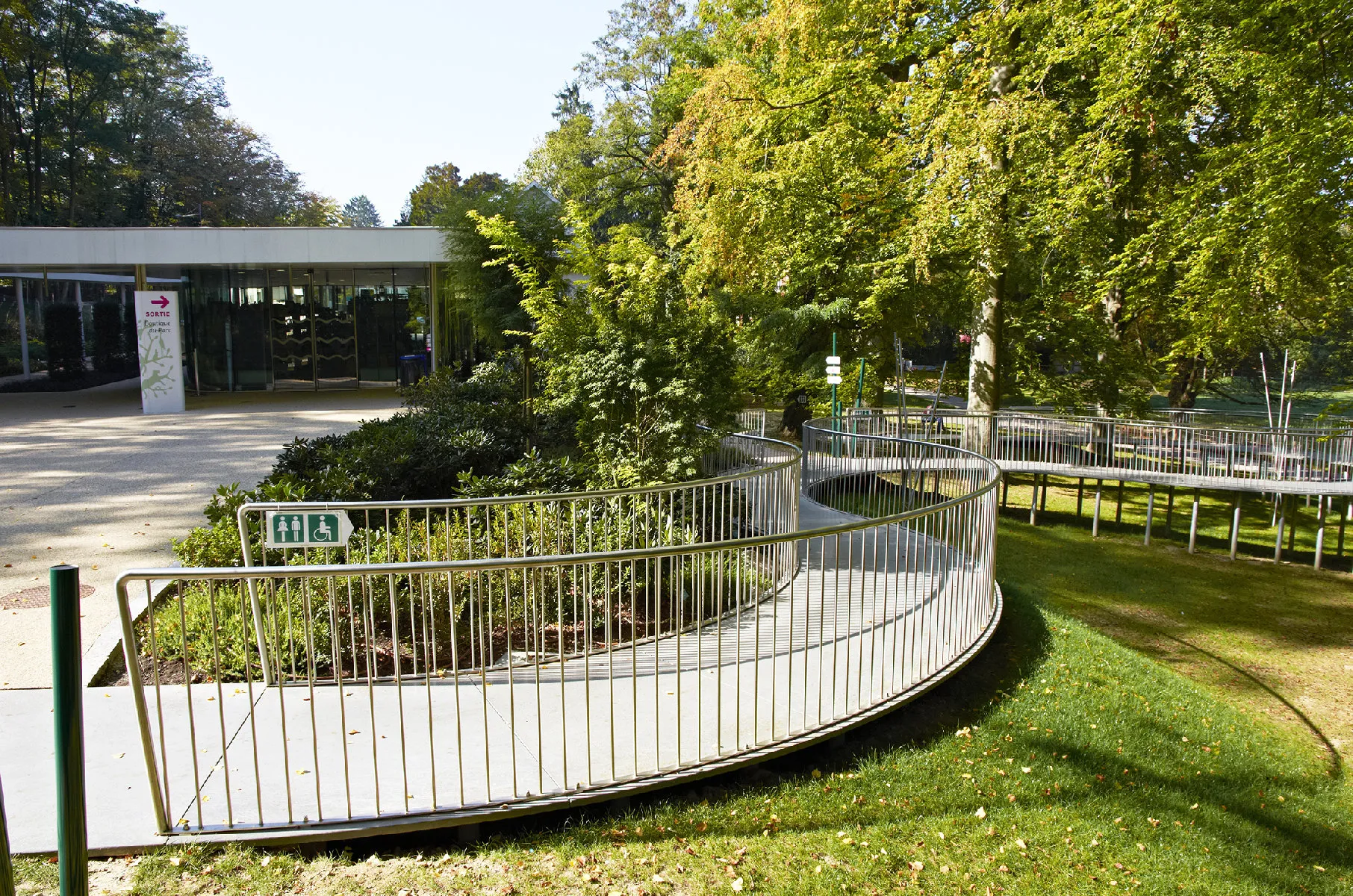 Passerelle piétonne sinueuse sur pilotis fins traversant un parc arboré